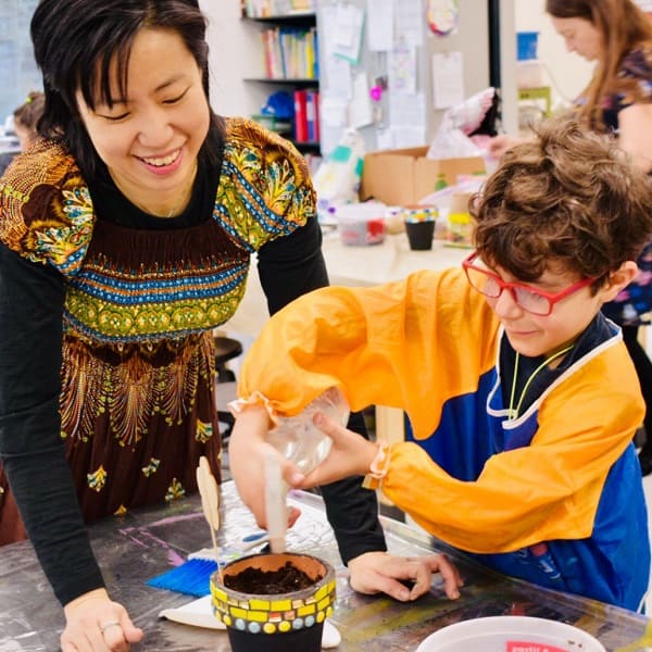 Artist with a child adding water to a decorated pot in a classroom